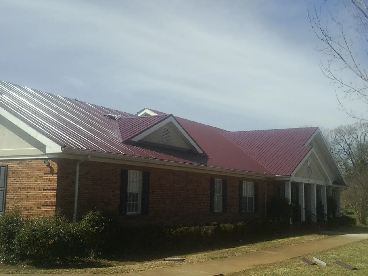 Red metal roof with gabled entries on a long brick building, from a Hail Damage Roof Repair job in Jewett City