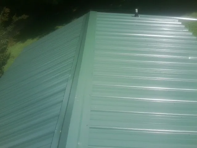 New green metal panels meeting at the ridge of a roof — Flat Roof Repair work by our crew in Jewett City