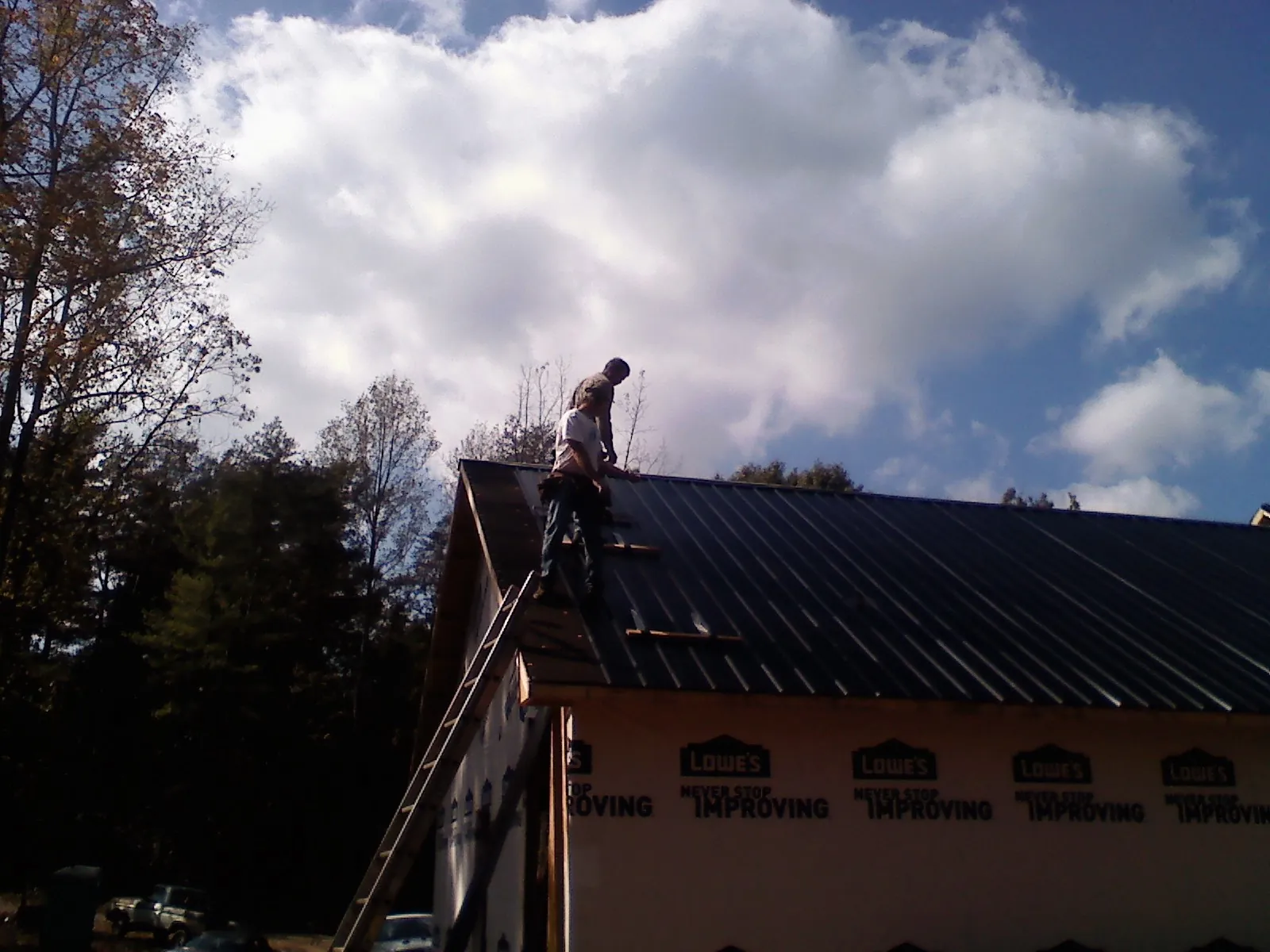 Roofer fastening dark metal panels high against a cloudy sky, from a Roof Inspection job in Jewett City