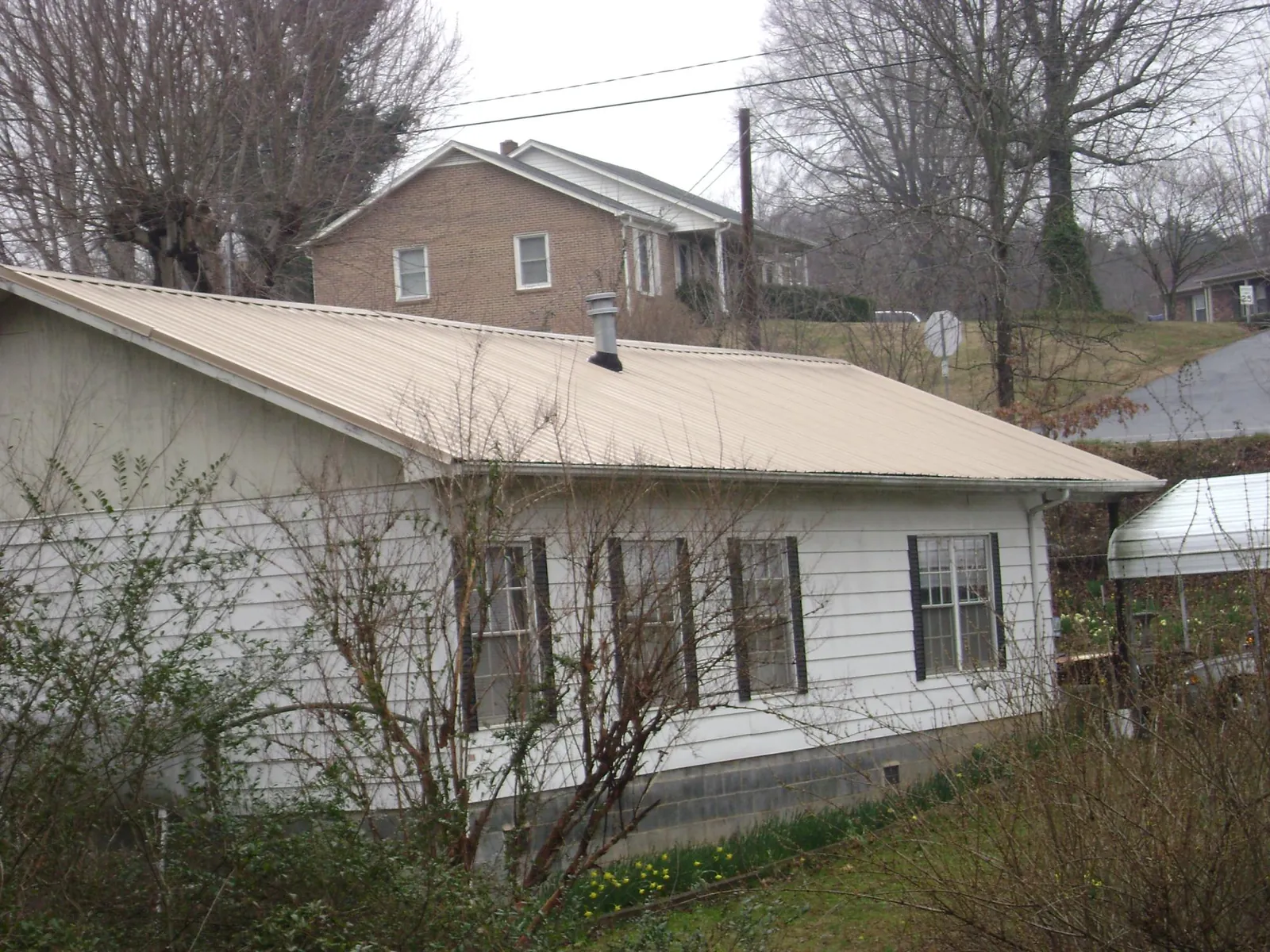 Tan metal roof on a white sided house set into a hillside — Commercial Roofing by Roofing Brothers in Jewett City